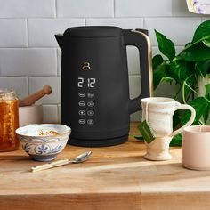 a black coffee pot sitting on top of a wooden table next to bowls and spoons