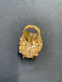 This vintage lady's showpiece ring is a true treasure. Made from 18k gold, it features a stunning oblong-shaped light yellow jade stone as the main attraction, accented by 58 white diamonds (.70 ct) and three emeralds (1 ct.). The patina light yellow color of the main stone adds a unique touch, while the intricate design of the ring makes it a true work of art. This ring is a size 5 and is branded by D.A.T, signed by Nuvill making it a must-have for any fine jewelry collection. Total weight 36+ grams. All measurements are approximated. One of the smaller emeralds reveals a chip upon close inspection. Gold Gemstone Rings For Evening, Luxury Yellow Rings For Collectors, Exquisite Gold Rings For Evening, Elegant Yellow Cabochon Rings, Luxury Gold Dome Ring With Cabochon, Luxury Gold Diamond Ring Collectible, Gold Diamond Ring With Cabochon For Gifts, Luxury Oval Collectible Rings, Elegant Oval Dome Ring Collectible