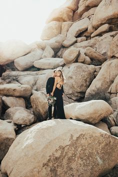 a woman standing on top of a large rock next to a pile of rocks and flowers