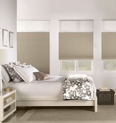 a white bed sitting in a bedroom next to two windows with blind shades on them