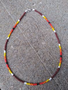 a red, yellow and white beaded necklace sitting on top of a stone floor