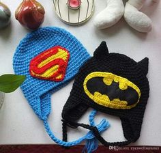 two crocheted hats with batman and superman logos are on a table next to stuffed animals