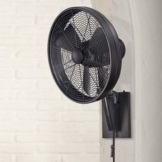 a black fan mounted on the side of a white brick wall