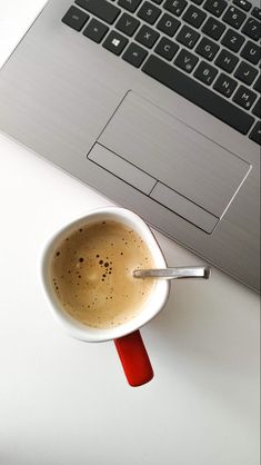 a cup of coffee sitting on top of a white table next to a laptop computer