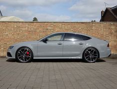 a grey car parked in front of a brick wall with black rims and red brake pads