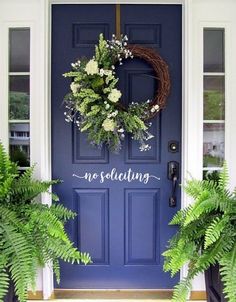 a blue front door with two plants and a welcome sign on the front porch area