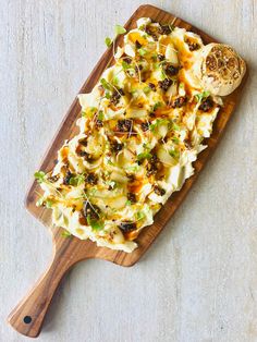 a wooden cutting board topped with food on top of a white table next to a spoon