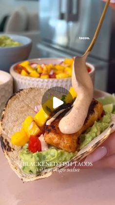 a person is holding a taco with chicken and vegetables on it in front of some bowls