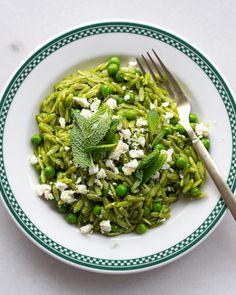 a white plate topped with green pasta and peas next to a silver fork on top of a table