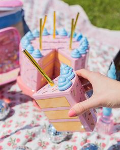 a person is holding a small pink cake with blue icing and straws on it