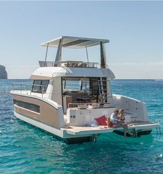 two people are sitting on the back of a boat in the blue water near an island