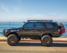 a large black truck parked on the side of a road near the ocean and water