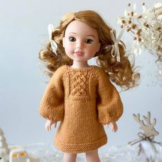 a doll with blonde hair wearing a brown sweater and white shoes, standing in front of snowflakes