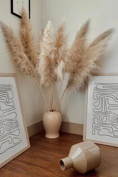 two framed pictures sitting on top of a wooden floor next to some pampas grass