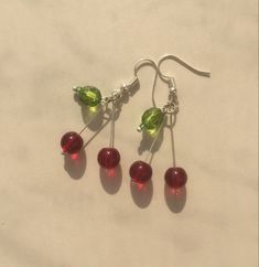 three red and green glass beads hanging from silver earwires on a white surface