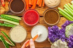 several different types of vegetables and dips on a wooden table with hands holding a carrot