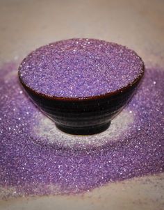 a black bowl filled with purple sand on top of a table