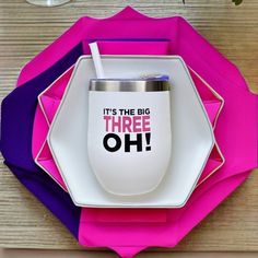 there is a white cup on top of a pink and purple place mat with the words, it's the big three oh