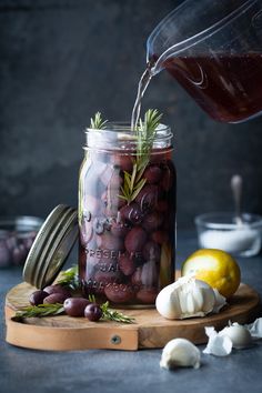 a mason jar filled with red wine and olives next to garlic, lemon, and rosemary