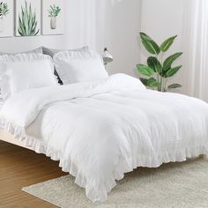 a bed with white linens and pillows in a small room next to a potted plant