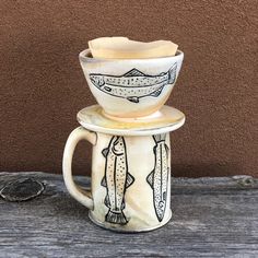 two mugs stacked on top of each other in front of a brown wall and wooden table