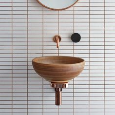 a wooden bowl sink in front of a round mirror on the wall above it is a black and gold faucet