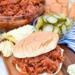 a pulled pork sandwich on a cutting board with pickles and celery next to it