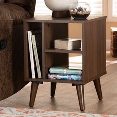 an end table with books and a vase on it in front of a couch next to a chair