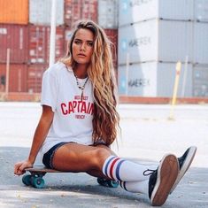 a woman sitting on top of a skateboard in front of shipping containers with her legs crossed