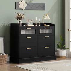 a black dresser with gold handles and drawers in a green living room, next to a white rug