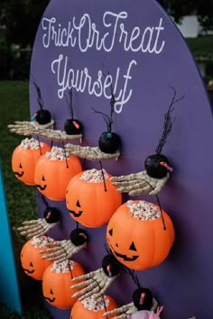 pumpkins are arranged on sticks in front of a sign that says trick or treat yourself