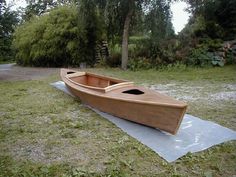 a wooden boat sitting on top of a piece of plastic in the grass next to trees