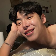 a young man laying on top of a bed next to a white wall and smiling at the camera