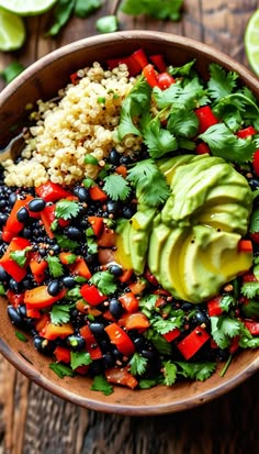 a wooden bowl filled with rice, black beans and avocado next to lime wedges