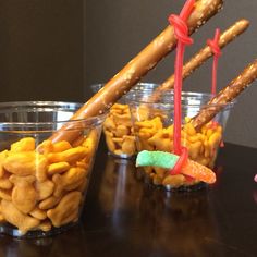 three plastic cups filled with candy and pretzels on top of a black table