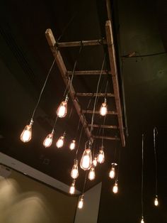 several light bulbs hanging from a wooden ladder in a room with dark walls and ceiling