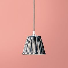 a light hanging from a metal pole on a pink wall with a black and white pleated lamp shade