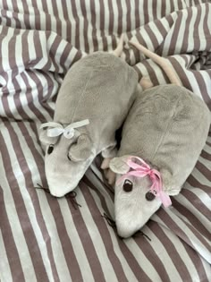 two stuffed animals are laying on a striped bed sheet with pink ribbon around their ears