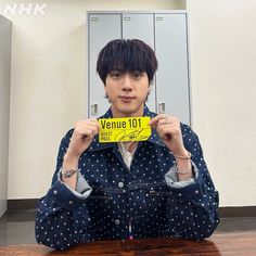 a young man holding up a yellow sign in front of his face while sitting at a table