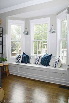 a white window seat with blue and white pillows on it in front of two windows