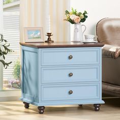 a blue chest of drawers in a living room next to a chair and vase with flowers