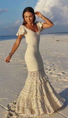 a woman is standing on the beach in a white crochet dress and sandals