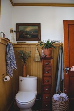 a white toilet sitting in a bathroom next to a wooden dresser and potted plant