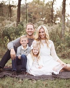 a family sitting on a blanket in the woods posing for a photo with their two children