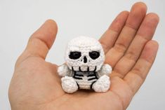 a small crocheted skeleton sitting on top of someone's hand in front of a white background