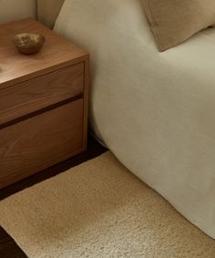 a bed with two pillows and a wooden night stand next to it on top of a carpeted floor