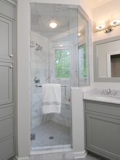 a white bathroom with marble counter tops and gray cabinets, along with a walk in shower