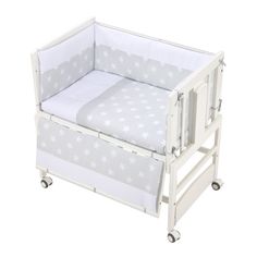 a white baby crib with stars on the sheets and bottom rail, in front of a white background