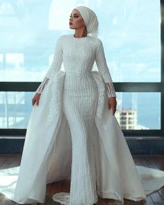 a woman standing in front of a window wearing a white gown and headpieces