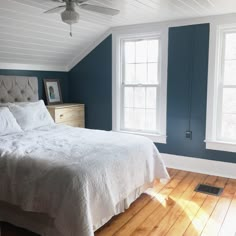 a white bed sitting under two windows in a bedroom